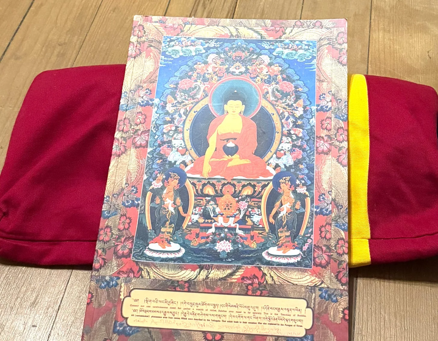 A printed Tibetan thangka of the Buddha resting on a red meditation cushion on a wooden floor